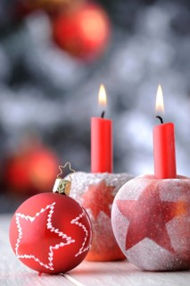 Red Christmas bauble with apples and candles in front of a Christmas tree