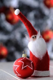 Red Christmas bauble and a felt Santa Claus in front of a Christmas tree