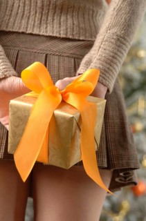 Woman in a mini skirt is holding gift wrapped in golden paper