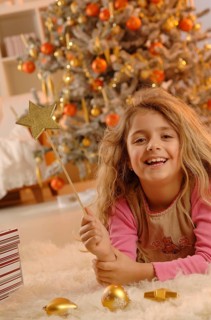 Smiling girl lying on the ground with a golden star and gifts in front of a Christmas tree