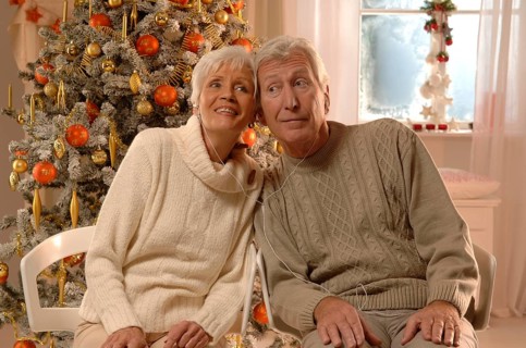 Mature couple with headphones sitting in front of a Christmas tree