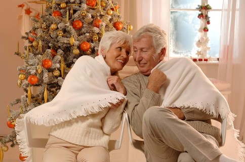 Mature couple in love wrapped in a blanked sitting in front of a Christmas tree