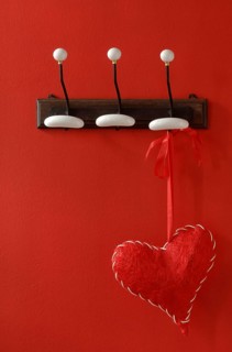 Red fabric heart hanging from nostalgic clothes hooks on a red wall