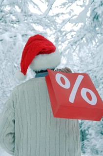 Man wearing a Santa hat in a snow-covered forest holding a shopping bag with a percent sign