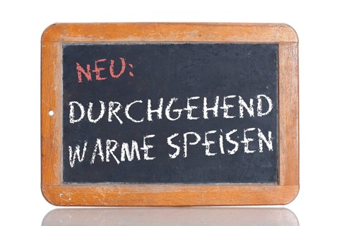 Old school blackboard with the words NEU: DURCHGEHEND WARME SPEISEN