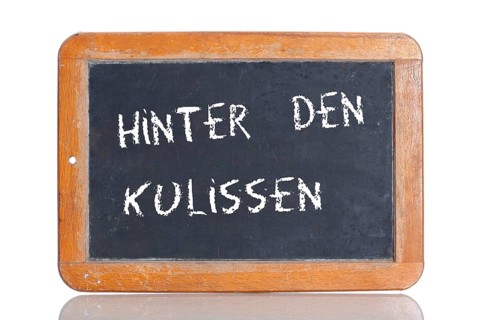 Old school blackboard with the term HINTER DEN KULISSEN