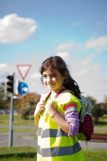 Girl with a school bag wearing a safety vest in front of a road sign