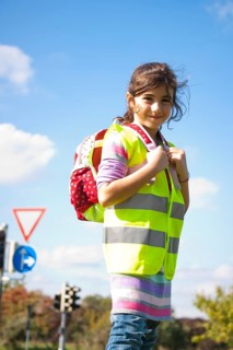 Girl with a school bag wearing a safety vest in front of a road sign