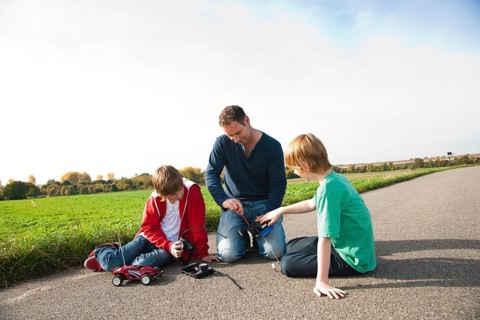 Father tinkering on a remote-controlled model car with his sons