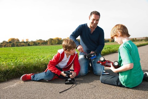 Father tinkering on a remote-controlled model car with his sons