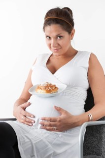 Pregnant woman holding hands on her stomach and resting a plate with a sweet bun on her belly