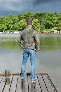 Man standing on jetty by a lake and looking at rainclouds