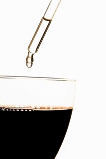 Pipette putting toxic substance in glass filled with red wine