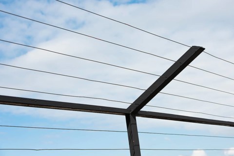 High fence with steel bars and wire against blue sky and clouds