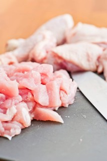 Cut up pieces of uncooked chicken on a plastic cutting board