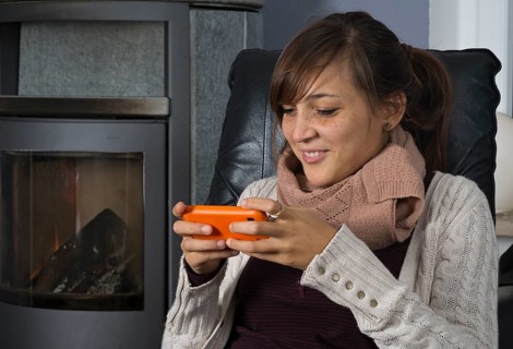 A young woman of Indonesian origin is sitting in front of a wood burner working on a smartphone