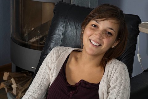 A young woman of Indonesian origin is sitting on a leather armchair in front of a wood burner