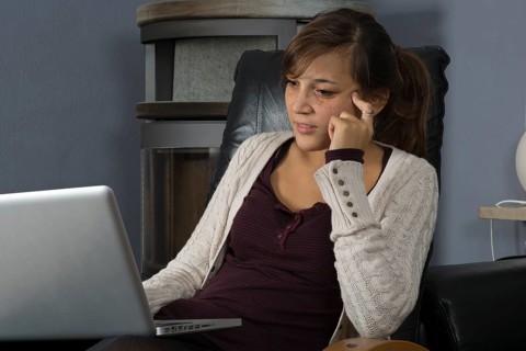 A young woman of Indonesian origin is sitting in front of a wood burner working on a laptop computer