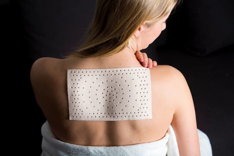 Young woman suffering from back pain has applied a heat plaster