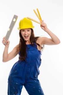 Woman wearing blue overalls and a hardhat holding a folding carpenter's ruler and a spirit level