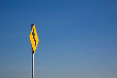Yellow traffic sign with a curved black 'S' arrow against a blue sky