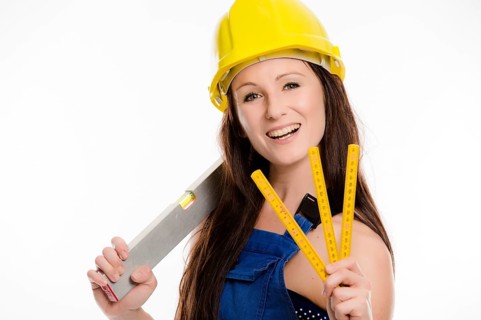 Woman wearing blue overalls and a hardhat holding a folding carpenter's ruler and a spirit level