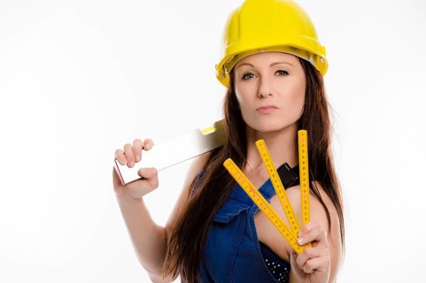 Woman wearing blue overalls and a hardhat holding a folding carpenter's ruler and a spirit level