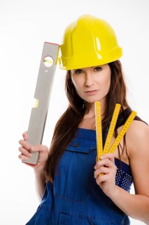 Woman wearing blue overalls and a hardhat holding a folding carpenter's ruler and a spirit level