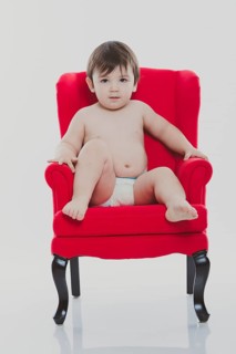 Young boy wearing a diaper sitting on a red chair