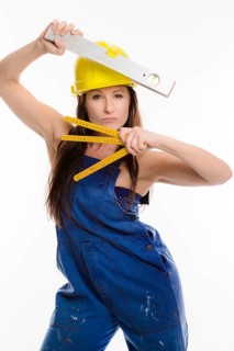 Woman wearing blue overalls and a hardhat holding a folding carpenter's ruler and a spirit level