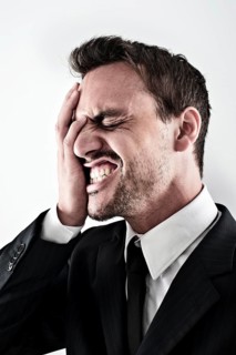 Desperate young man wearing a suit covering his face with his hand