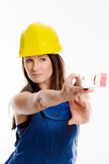 Woman wearing blue overalls and a hardhat holding a spirit level