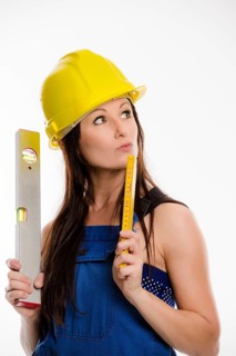 Woman wearing blue overalls and a hardhat holding a folding carpenter's ruler and a spirit level