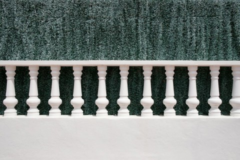 A white stone balustrade in front of an artificial green hedge