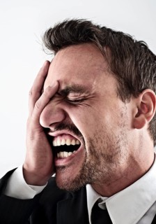 Desperate young man wearing a suit covering his face with his hand