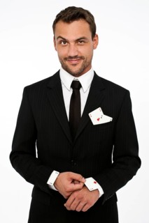 Man wearing a suit pulling an ace of diamonds out of his sleeve with other aces in his pocket