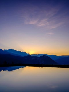 Mountain silhouettes are reflected in an artificial mountain lake at sunset
