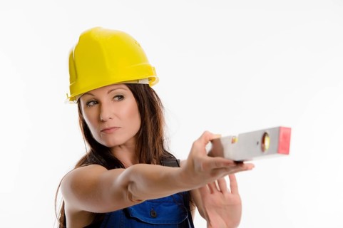 Woman wearing blue overalls and a hardhat holding a spirit level
