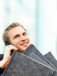 Businessman carrying ring binders while using a mobile phone