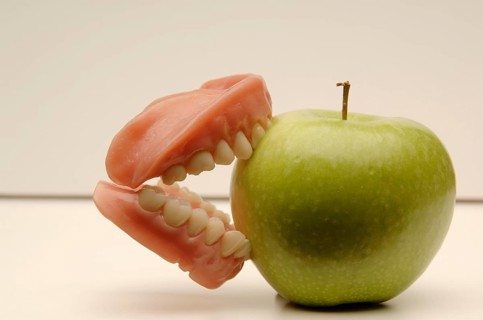 Dentures biting into a green apple
