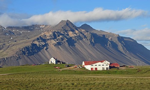 Farm and mountain scenery with eroded scree slope in the evening light near Hofn