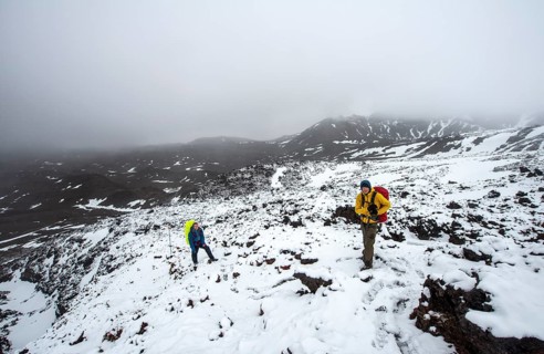 Hikers on hiking trail Tongariro Alpine Crossing in snow over lava fields