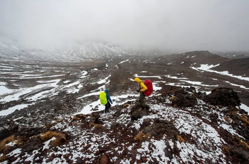 Hikers on hiking trail Tongariro Alpine Crossing in snow over lava fields