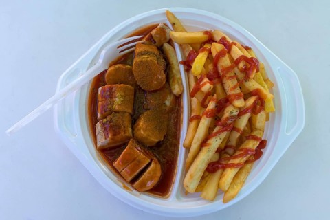 Currywurst with French fries with plastic fork on a plastic plate