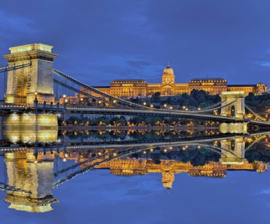 Chain bridge in front of castle palace with reflection in the Danube