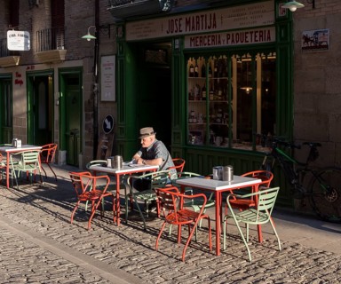 Old man reads newspapers and drinks coffee at a cafe table in early morning
