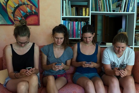Four young woman sitting on a sofa chatting with their smartphones
