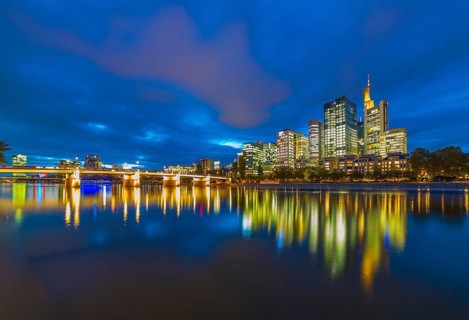 Skyline of Frankfurt with illuminated skyscrapers and Untermainbrucke bridge with water reflections in Main