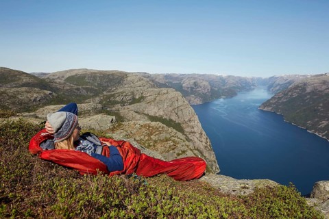 Young woman in a red sleeping bag with view over the fjord