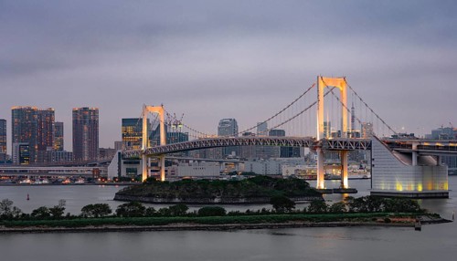 View of skyline with skyscrapers and illuminated Rainbow Bridge in the evening